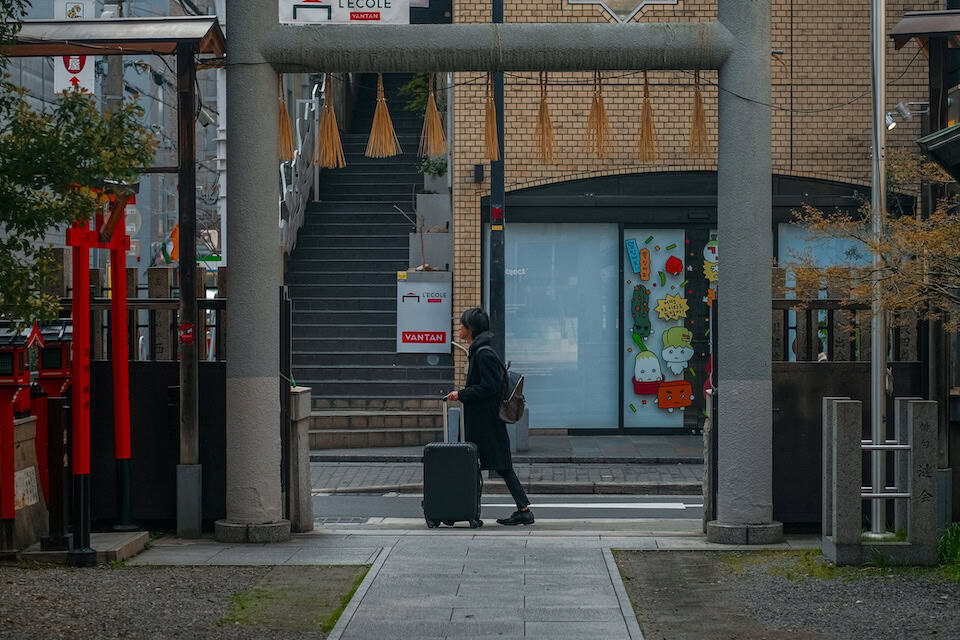 Hombre pasando por un torii con una maleta